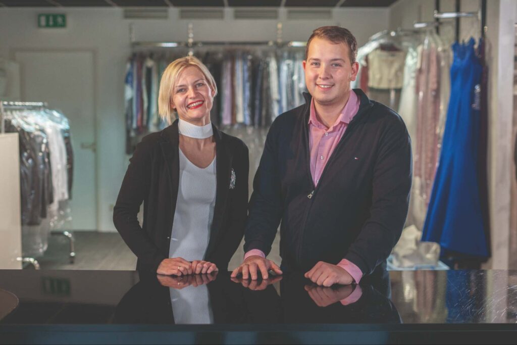 Das Team: Zwei Personen am Tresen mit gebügelter Wäsche im Hintergrund.