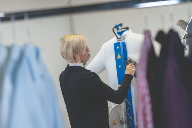 Frau bügelt Hemd auf senkrechter Bügelstation mit silbernem Eisen.