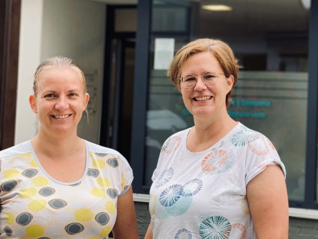 Zwei Frauen stehen lächelnd vor der Physiotherapiepraxis Bodner & Leven