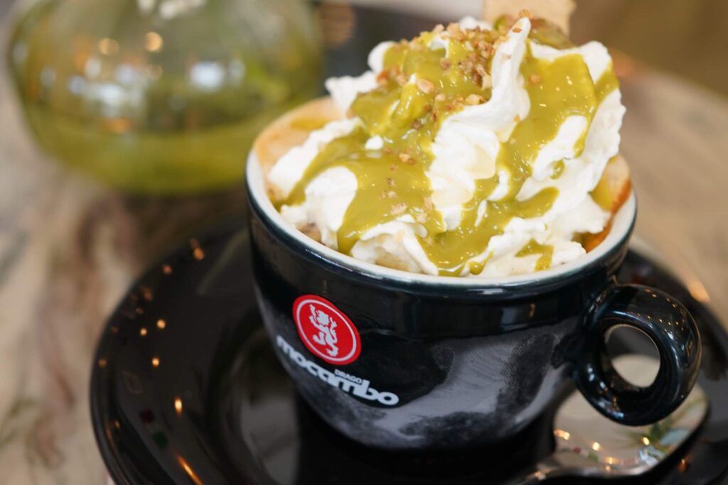 Schwarze Tasse und Untertasse mit Pistazien Cappucino. Sahnehaube und Pistaziencreme.