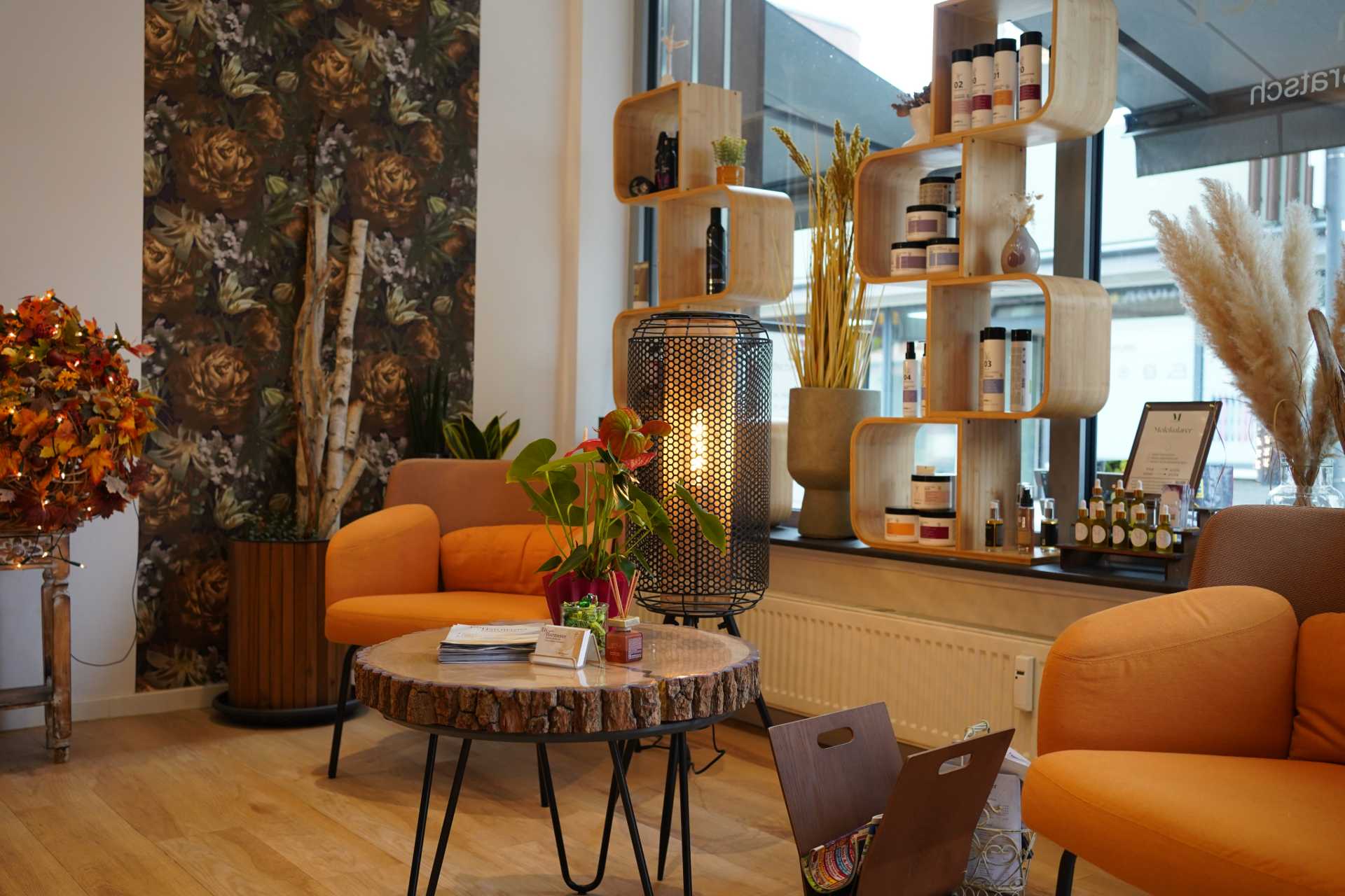 Wartebereich des Friseurladens mit orangenen Sesseln, rundem Holztisch und herbstlicher Dekoartion